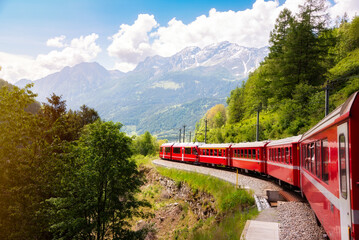 Red train moving in beautiful green summer forest in Switzerland