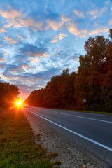 Asphalt road in motion with trees against a night sky with bright sunset