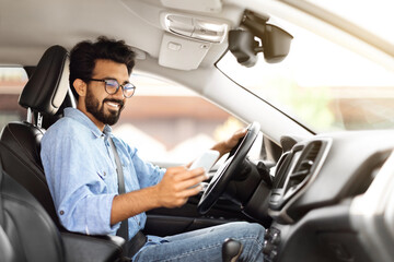 Happy young indian guy using smartphone while driving car