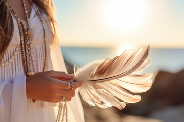 Woman with boho jewellery holding a feather in her hands close up. Spirituality, harmony and connection with nature concept.