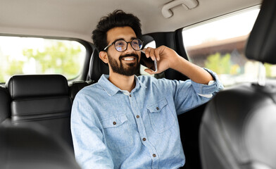 Smiling young indian man talking over phone, sitting in taxi
