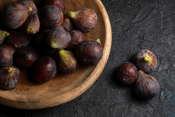 Fototapeta premium Higos maduros frescos de la variedad Bordissot Negra Rimada en un plato de madera sobre fondo negro