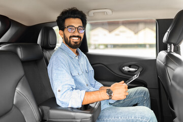 Handsome indian businessman sitting in car taxi, using digital tablet