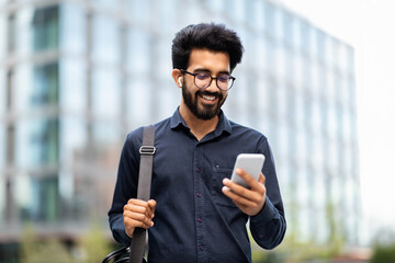 Happy eastern man manager going to office, using phone