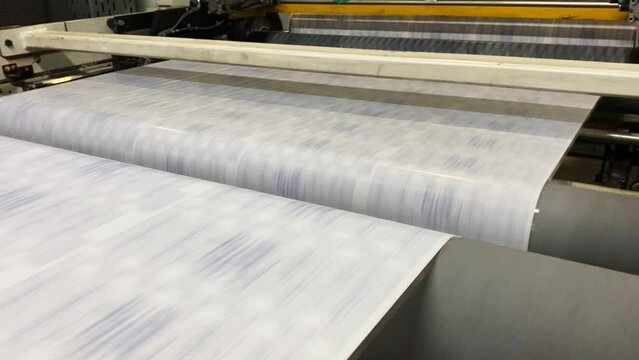 Flexographic printing on plastic film. Printing. Large roll rotates quickly. Film rotates between the shafts. Roller machine prints.