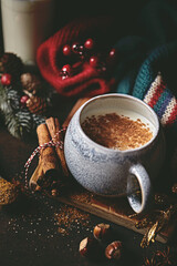 Hot milk with spices, warm shawl and Christmas decorations on rustic background. Copy space