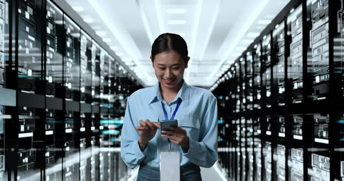 Asian Woman Working In Server Room Database. Smiling And Shaking Head While Using Smartphone Managing Supercomputer Network

