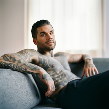 Muscular man with tattoos on his chest and shoulders relaxes on a sofa, ai art