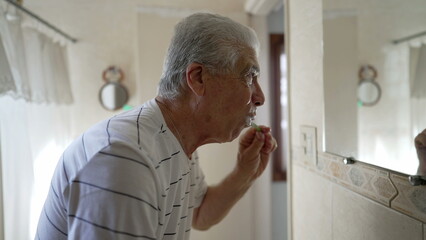 Fototapeta premium Casual Domestic Scene of Elderly Man Brushing Teeth as Part of Morning Routine. older person dental hygiene and washing face, starting the day ritual