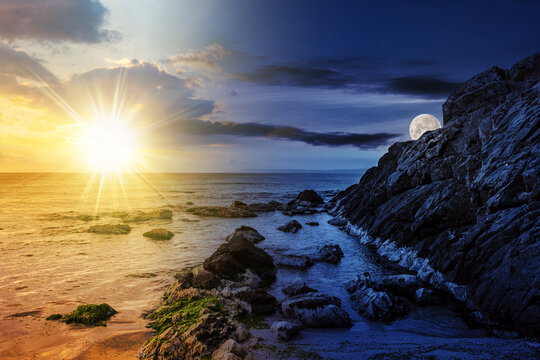 large boulders and seaweed on the rocky coast of the sea with sun and moon at twilight. day and night time change concept. mysterious countryside scenery in morning light
