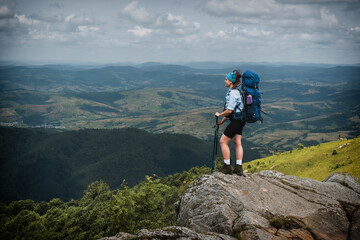 Girl hiker with a backpack stands on a rock in the mountains. Trekking life. Hike through the Carpathian mountains. Green mountain slopes