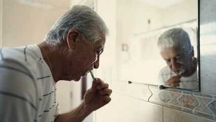 Senior morning routine brushing in mirror while staring at his own reflection in bathroom miror. Dental hygiene, elderly person starting the day - obrazy, fototapety, plakaty