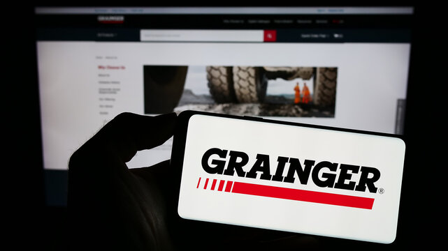 Stuttgart, Germany - 08-12-2023: Person holding smartphone with logo of US industrial supply company W.W. Grainger Inc. on screen in front of website. Focus on phone display.