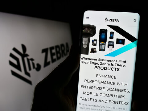 Stuttgart, Germany - 08-13-2023: Person holding cellphone with webpage of US company Zebra Technologies Corporation on screen in front of logo. Focus on center of phone display.