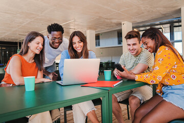 Group of multicultural teenage students working on a project using a laptop computer on a high school library. Young friends studying on a university class. Academic team learning doing the homework