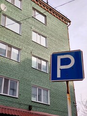 Multi-storey brick house with a parking space sign. Urban high-rise building in green color,