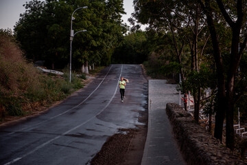 Young woman in sportswear is jogging early in morning on green track at sunrise. Pursuit of goals