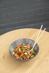 A bowl of udon noodles, veal and fried vegetables angle view on wooden table