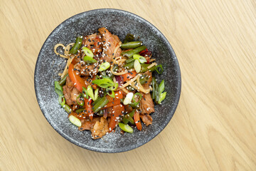A bowl of udon noodles, veal and fried vegetables top view on wooden table