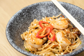 Udon noodles with shrimp and fried vegetables in a bowl top view