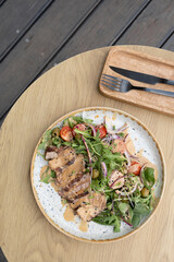 A plate with veal meat on greens with vegetables and olives under nut sauce on a wooden table top view