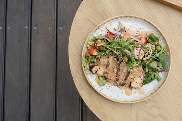A plate with veal meat on greens with vegetables and olives under nut sauce on a wooden table top view