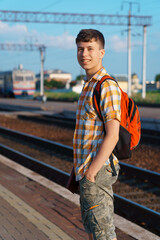 a student poses at a railway station, a teenage boy walks along the platform to the train, he has a backpack and books, goes to study, the concept of education