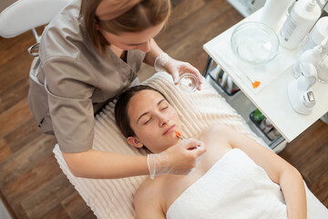 Top-down shot of a doctor applying gel for opening pores on face of a client of a cosmetology clinic before ultrasound or mechanical cleaning. Modern way of cleaning skin in cosmetology clinic