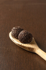 two brazilian brigadeiro (brigadier) with chocolate sprinkles on a wooden spoon over wooden table. traditional brazilian candy for party dessert