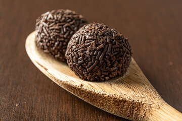 two brazilian brigadeiro (brigadier) with chocolate sprinkles on a wooden spoon over wooden table. traditional brazilian candy for party dessert