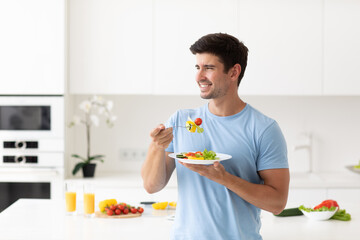 Young man eating fresh salad at kitchen home