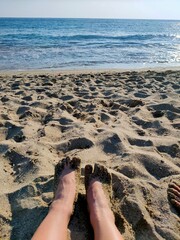 Women's feet on the sea beach, in the sand.