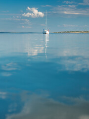 alone white sailboat on the calm water with reflections of clouds