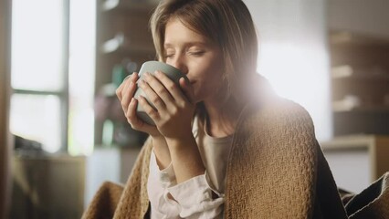 Portrait of charming blond young woman under the blanket take sip drinking hot tea or coffee sitting on couch at home Calm relaxed female enjoying weekend leisure time alone indoors