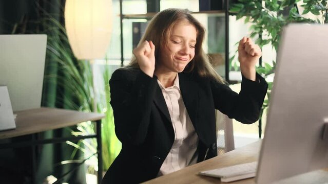 Positive tired young businesswoman feels satisfied with work well done at light modern office Calm woman employee relax and dance after hard working day finished project on computer indoors