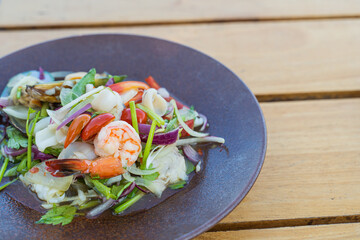 Spicy seafood salad, popular food on a wooden table, appetizing in a cafe next to the sea, Sue Flamingo, Ao Yon Beach, Phuket Thailand