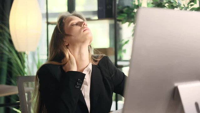 Overworked tired young businesswoman with severe neck shoulder pain after hard work on computer at modern office Sad female suffers from tension in the spine indoors