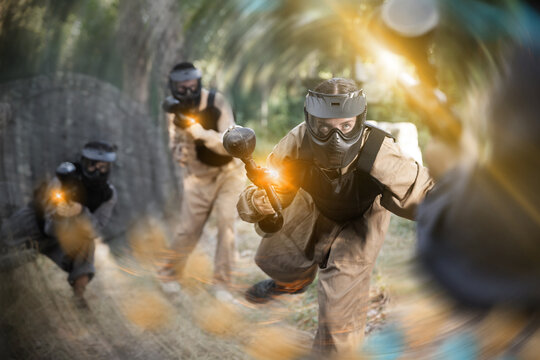 Young woman paintball player wearing protective clothes and helmet, rushing through enemy lines, shooting with paintball marker.