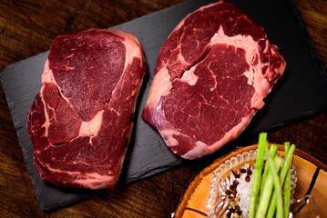 Two ribeye steaks with salt and pepper on the black cutting board background.