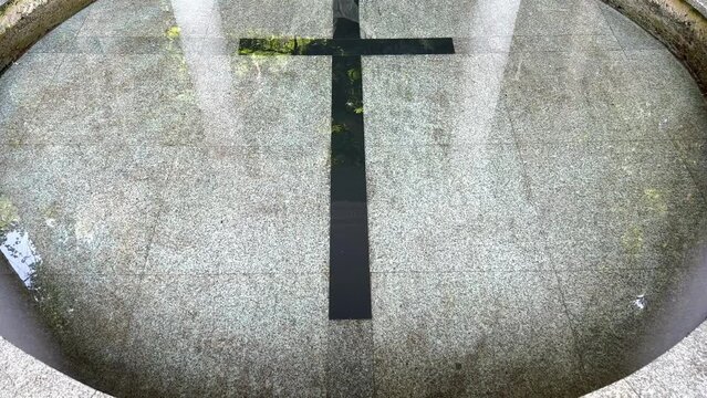 A large black Christian cross underwater in a well or pool of clear water. Crucifixion in water, water consecration ceremony. Religious crucifixion in water. Holy water. Black cross.