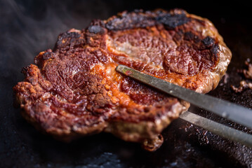 Close up of beef steaks cooking on grill in backyard barbecue.