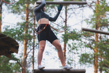 View of high ropes course, process of climbing in amusement acitivity rope park, passing obstacles and zip line on heights in climbing safety equipment gear between the trees om heights, summer day