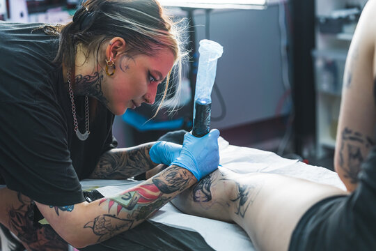 Young artist during a tattoo session. Tattooed female artist drawing a leg tattoo. Art in many forms. Indoor shot. High quality photo