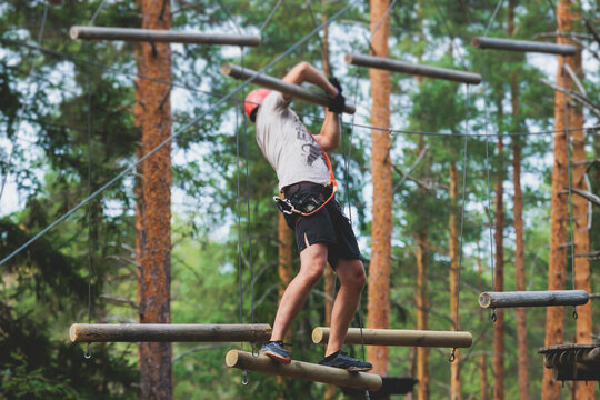 View of high ropes course, process of climbing in amusement acitivity rope park, passing obstacles and zip line on heights in climbing safety equipment gear between the trees om heights, summer day - Powered by Adobe