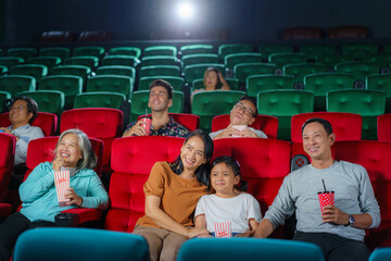 Asian family father, mother, son and grandmother watching movie at the cinema happily on weekends..
