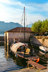 Italy, Lake Lugano. View of the lake, old houses and boat pier. An old pleasure boat, decorated with colorful flags, stands at the pier.