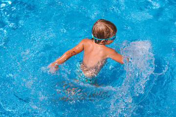 little boy swims in the pool in swimming goggles