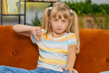 Dislike. Upset girl showing thumbs down sign gesture, expressing discontent, disapproval, dissatisfied bad work at modern home apartment indoors. Displeased teen child, kid in living room on sofa