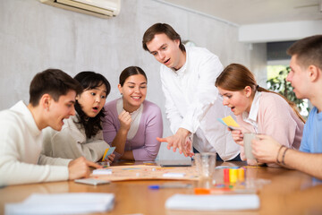 Portrait of cheerful emotional young guy spending free time with friends in student campus, playing...