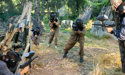 Fototapeta premium Group of friends paintball players of opposite teams in shootout in forest outdoors